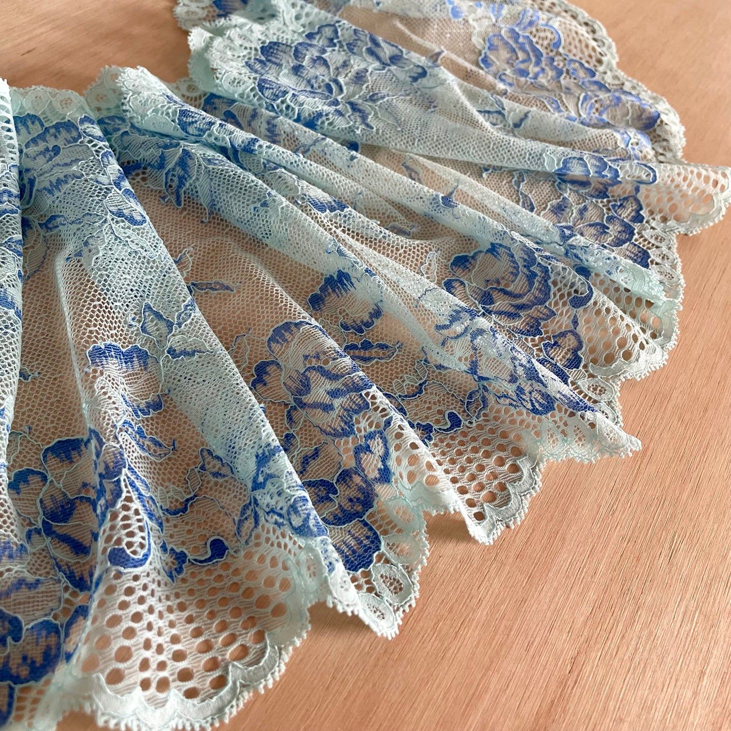 Light blue floral lace trim with scalloped edges, displayed in a layered fan shape on a light wood surface.